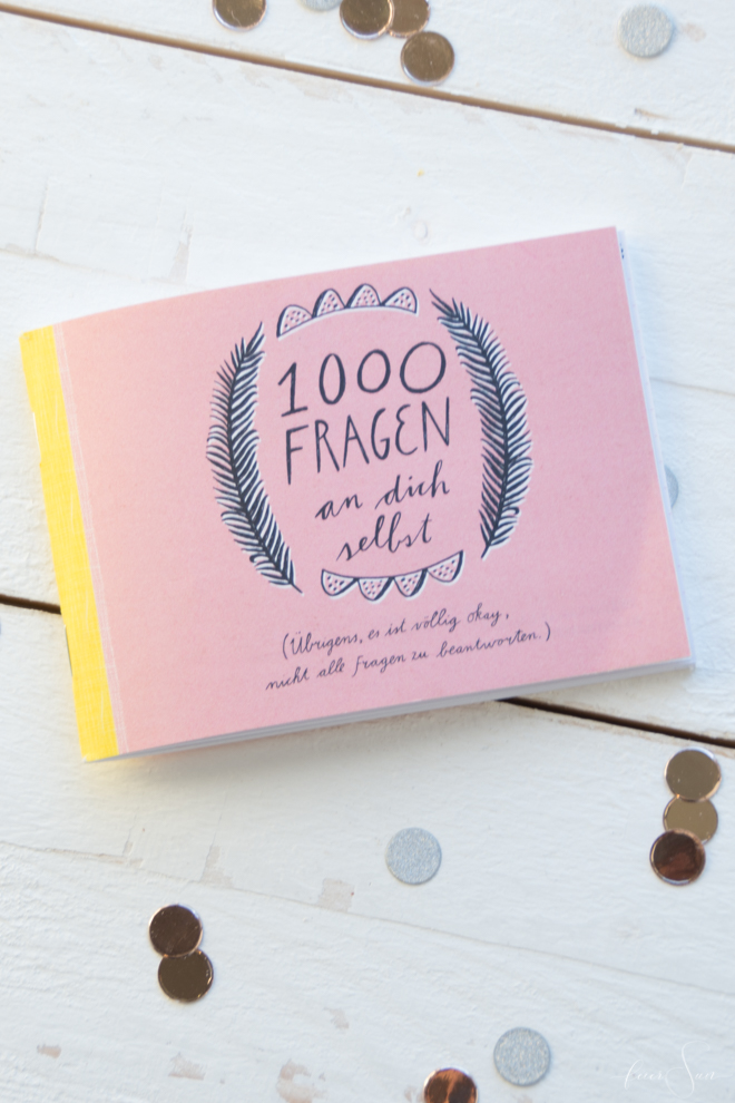 Das Büchlein 1000 Fragen an dich selbst aus dem Flow-Magazin. Im Hintergrund goldenes Konfetti. 