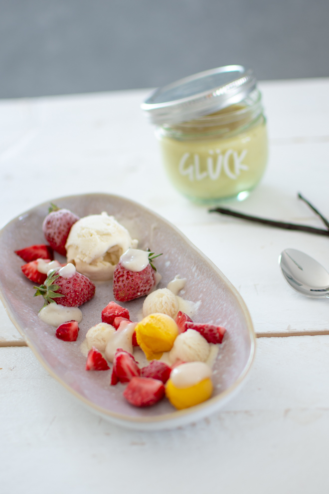 Vegane Vanillesoße auf Sorbet mit Erdbeeren auf einem Teller angerichtet dazu kommt Kokos-Vanille-Eis und die Soße ist in einem Glücks-Glas mit der Aufschrift "Glück"