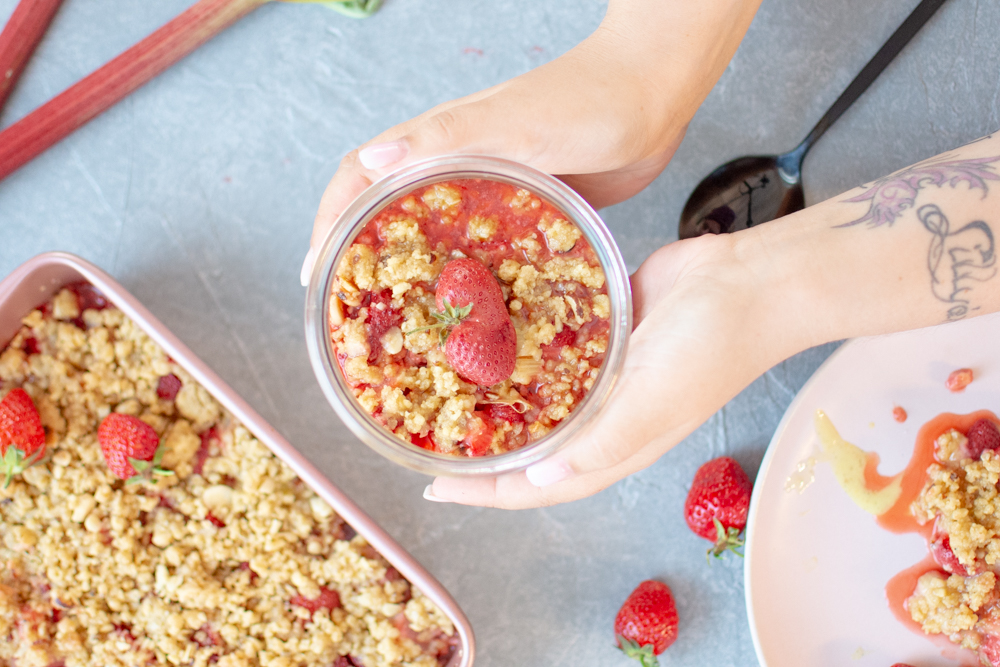 Erdbeer-Rhabarber-Crumble fertig fotografiert im Glas mit händen umklammert.