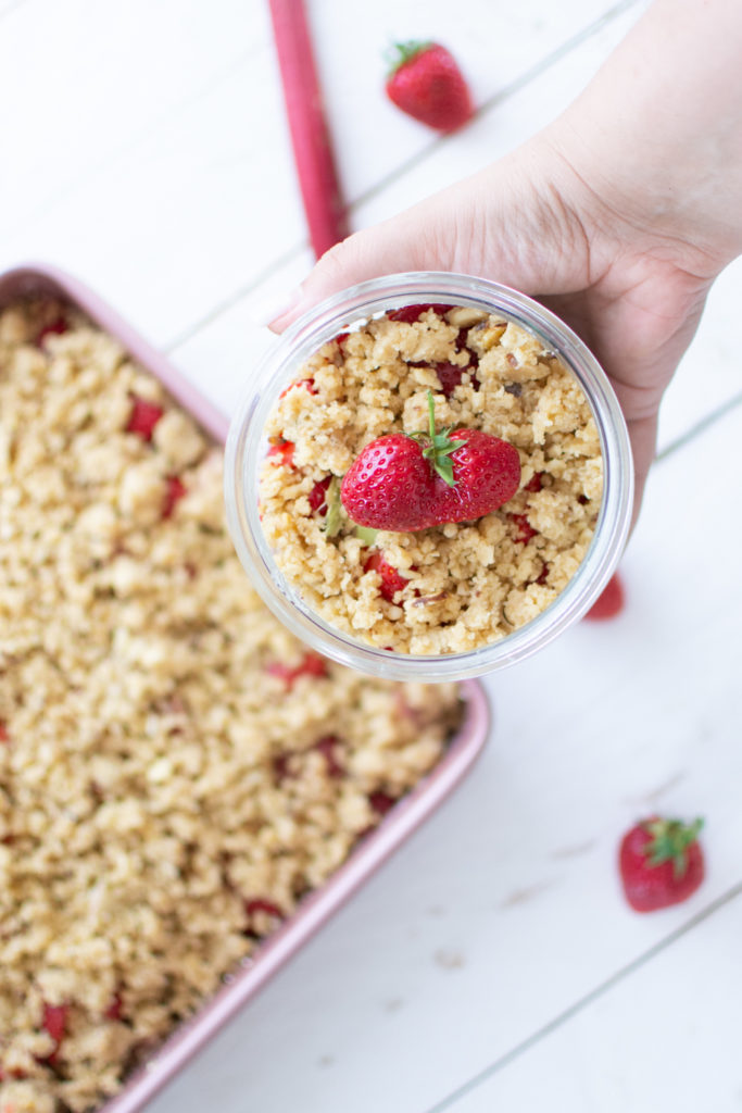 Erdbeer-Rhabarber-Crumble fertig fotografiert im Glas mit händen umklammert.